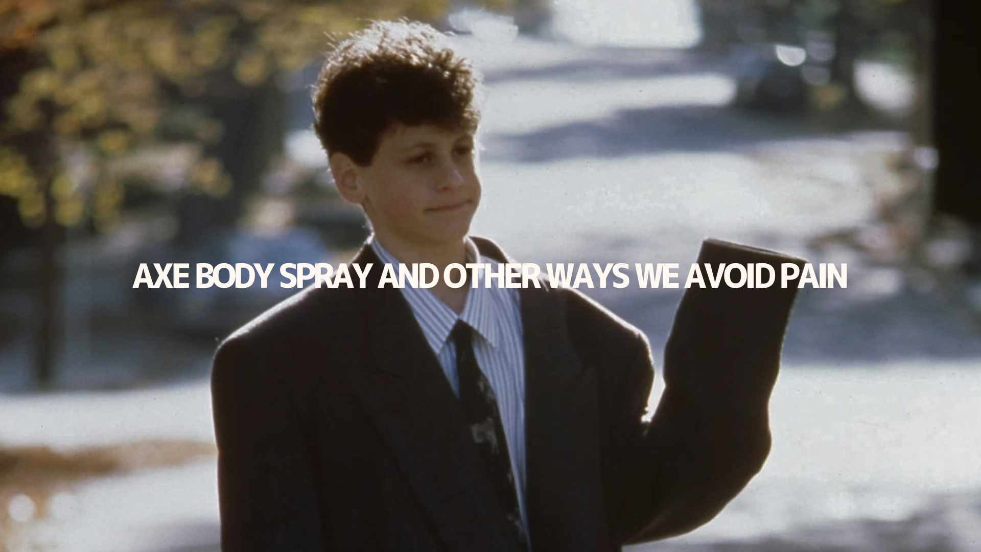 A young person in a suit outdoors, with the title Axe Body Spray and Other Ways We Avoid Pain across the image